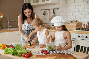 Family prepares lunch in the kitchen. Mom teaches her daughter and son to prepare a Salad of fresh vegetables. Healthy natural food, vitamins for children