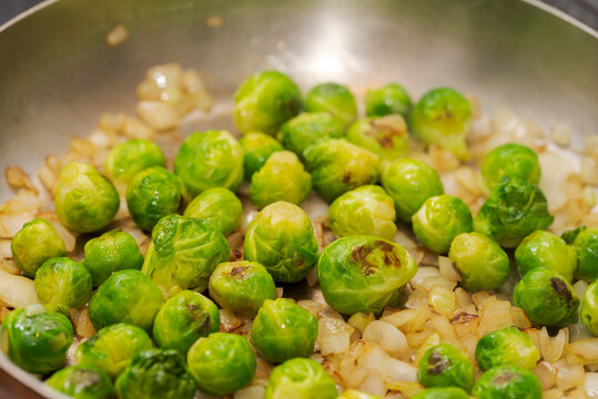 Detail of whole fresh green organic brussels sprouts frying in stainless steel pan with onion cubes