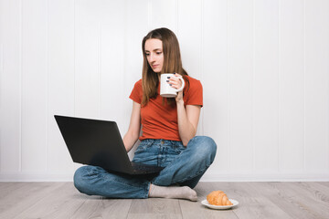 Smiling girl holding laptop computer while sitting on a floor with cup of tea