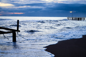 View from beach to water of sea, waves with white foam, pierce and sky with clouds in a nice evening.