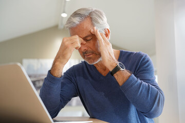 Senior man having a headache while working on laptop computer - 404463059