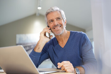 Portrait of senior man with blue shirt talking on phone at home