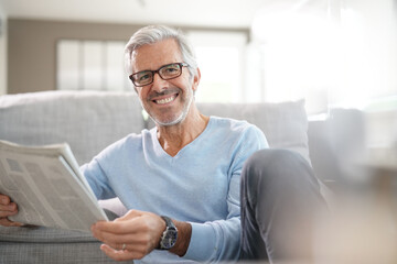 Attractive senior man with eyeglasses relaxing at home reading newspaper - Powered by Adobe