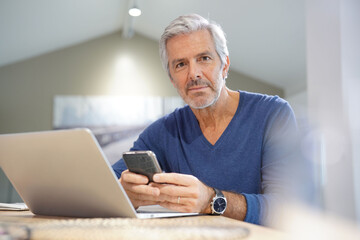 Portrait of senior man with blue shirt using smartphone and laptop