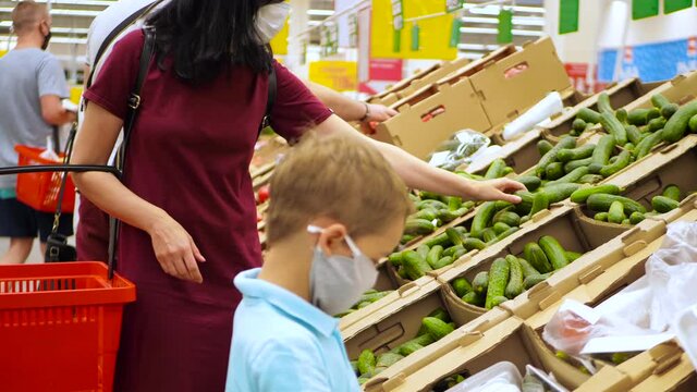 A mother and child in medical masks are shopping in a supermarket. A woman and a little boy in the vegetable department. Social distance the second world war the time of a pandemic.