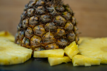 Front view at the fresh healthy slieced to triengels pineapple fruit with non peeled pineapple in the middle on black desk with wooden background