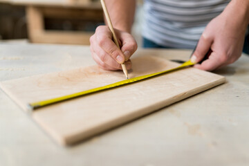 Close-up of man worker's hand measuring a wooden board with a ruler with scale