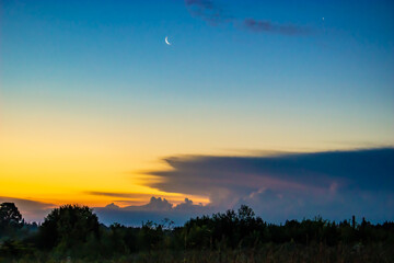 The moon is hovering over the earth, and the dawn is approaching and the glow highlights the clouds hanging in the sky.