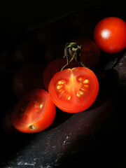 Tomates cherry uno cortado a la mitad sobre pizarra y con fondo negro
