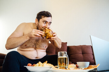 portrait of a caucasian fat man eating chicken grill on the sofa. looking at camera, at home....