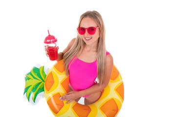 A young woman in a pink swimsuit and glasses holds an inflatable swimming circle and drinks lemonade