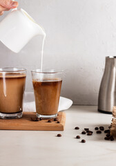 Coffee with milk on wood board. Woman pouring steamed milk into coffee glass cup.