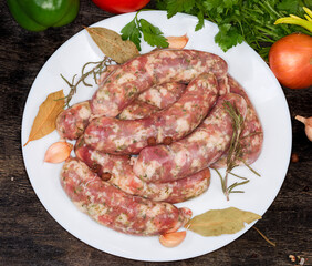 Uncooked homemade pork sausages and spices on dish, top view