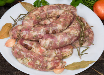 Uncooked homemade pork sausages and spices on dish, close-up