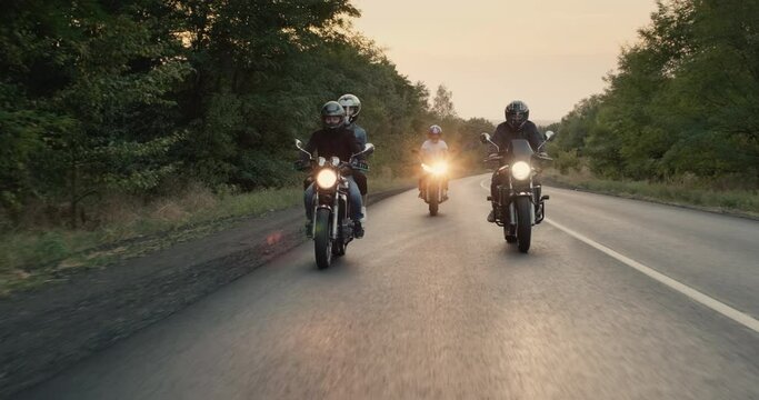 Bikers ride motorcycles with lights turned on, the road goes through the forest