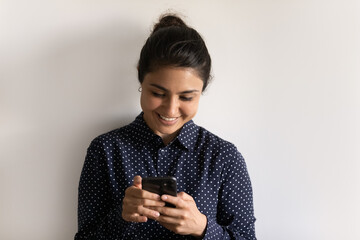 Happy Indian young woman isolated on grey studio background look at smartphone screen text or...
