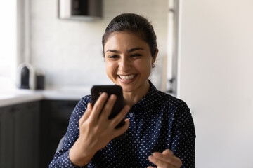 Overjoyed young Indian woman look at smartphone screen talk on video call on gadget. Smiling...