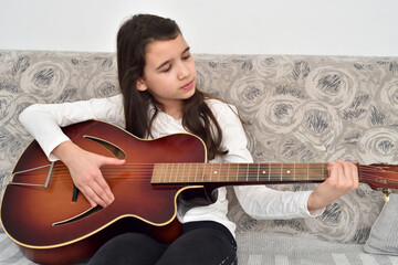 Young girl playing the guitar. Child sitting on the sofa and practicing on the vintage acoustic...