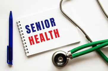 SENIOR HEALTH is written in a notebook on a white table next to pen and a stethoscope.