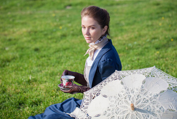 Romantic young beautiful lady on a picnic with a cup of tea outdoors. Victorian style vintage