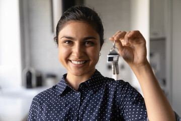 Close up portrait of smiling millennial Indian woman hold show keys to new house. Excited young...
