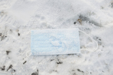 disposable medical mask with ear loops, sprinkled with snow on snowy ground