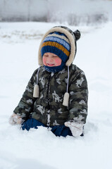 Little boy playing in the snow on the street. Kid with red cheeks in the snow