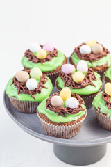 Homemade carrot cupcakes with cream cheese frosting and Easter chocolate eggs, on gray cake stand, vertical, copy space