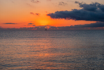 Sunrise with the red orange sun raising up from the sea with dark clouds at beach Spiaggia di Santa Maria Navarrese, Sardinia, Italy
