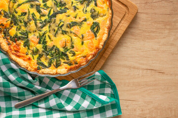 Top view on seafood and salmon fish quiche pie with baby spinach leaves- homemade recipe pie served on wooden table background with copy space, selective focus