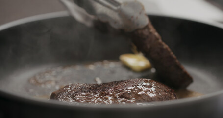 man flipping beef steak on nonstick pan with tongs