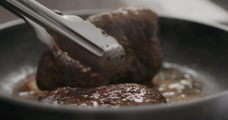 man flipping beef steak on nonstick pan with tongs