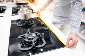 Obraz na płótnie Canvas Male hand interior designer using tape measure on gas stove on modern countertop in kitchen showroom. Shopping appliance for domestic kitchen. Home improvement concept 