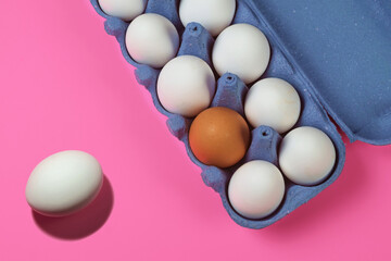 Brown egg between white eggs in a paper tray on a pink surface