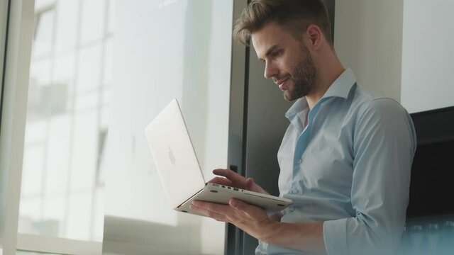 A focused young businessman is using his laptop computer standing in the kitchen at home