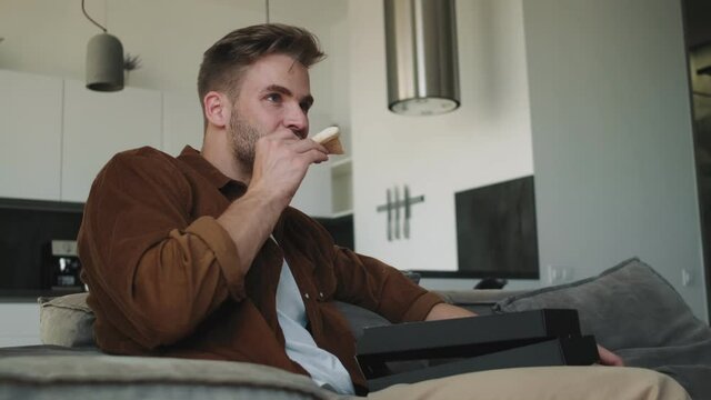 A Pleased Young Man Is Eating Pizza While Watching Tv Sitting At Home