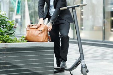 Cropped image of businessman standing next to his electric scooter and searching for document in his leather bag