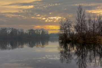 Fototapeta premium Dawn by the reservoir. The forest along the river is reflected in the water. Tranquil nature scene.