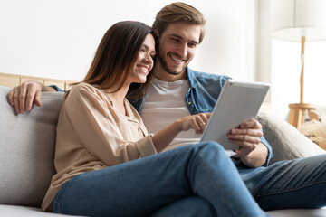 Obraz premium Young couple sitting on couch at home, using a tablet PC for Internet and social media.