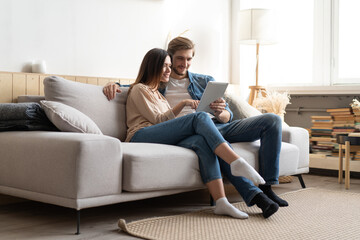 Young couple sitting on couch at home, using a tablet PC for Internet and social media.