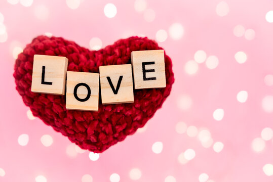 Words love on a red plush heart blurred pink background with copy-space with bokeh from a golden garland and lights. Holidays concept of mothers day, fathers day, christmas, valentines day and romance