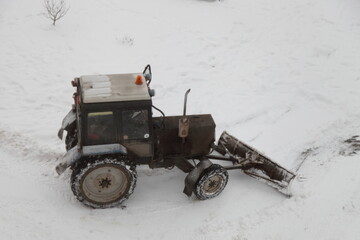 Obraz premium Old Soviet wheeled tractor with a scraper removes snow on the street after a snowfall on a winter day top side view, city utilities
