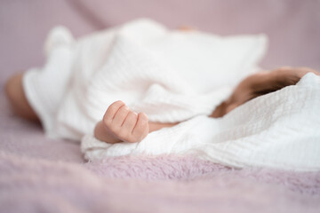 close up small hand of baby infant sleeping on soft bed covered with white cloth. little baby fingers in fist.