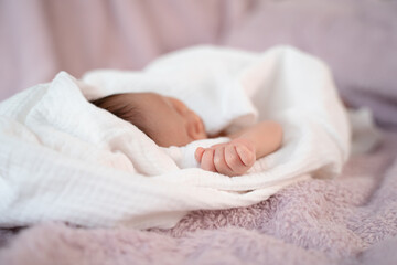 Fototapeta na wymiar close up small hand of baby infant sleeping on soft bed covered with white cloth. little baby fingers in fist.