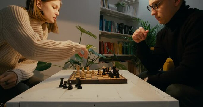 Couple Play Chess at Home at Night. Lady wins by checkmate. Sport and Hobby at quarantine or isolation during Lockdown. Man and Woman move chess pieces on chessboard. 4K Medium Zoom Out Shot