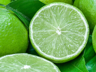 Obraz na płótnie Canvas green lemons with half cut and leaves a sour fruit ingredient for healthy food and juice or beverage by closeup texture of limes for cuisine and nature background