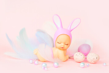 small baby doll with rabbit ears and painted eggs on a pink background, the concept of a greeting card for Easter