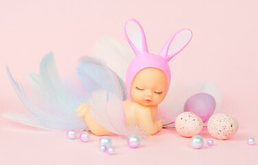 Obraz na płótnie Canvas small baby doll with rabbit ears and painted eggs on a pink background, the concept of a greeting card for Easter
