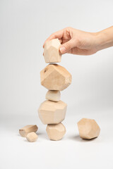 Tumi-ishi puzzle game. A woman or a girl places her hand on another block of wood on top of an unstable tower. The process of the game. Stones for Rock Balance.