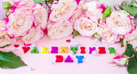 delicate bouquet of bushy peony roses, pearls and wooden colorful letters Valentines day on a pink background